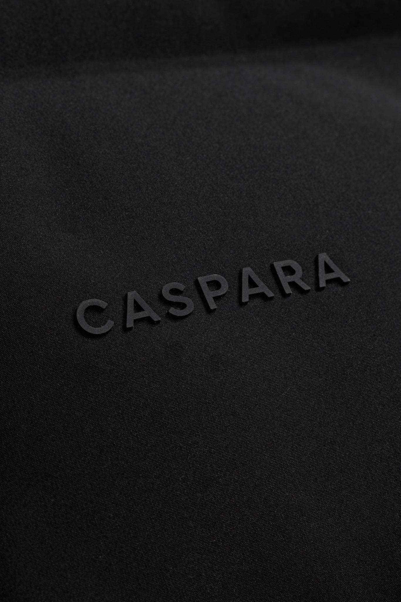 Close-up of the black embossed CASPARA logo on a quilted black puffer vest.